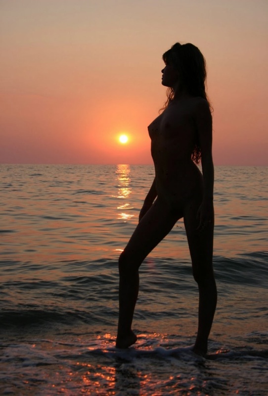 Молодая девушка позирует в море на фоне заката 3 фото